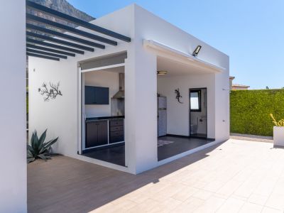 Cuisine extérieure moderne et espace barbecue avec des meubles sombres, intégrant une salle de bain extérieure pratique, sur une terrasse carrelée avec vue sur la montagne.