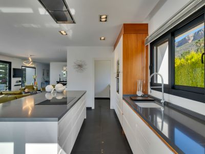 Cuisine ouverte moderne avec plans de travail en quartz gris, armoires blanches sans poignées, plaque à induction intégrée sur l'îlot et vue sur la montagne depuis la fenêtre.
