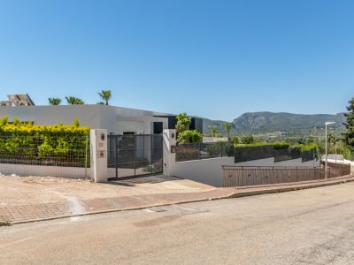Extérieur de la villa moderne avec portail d'entrée, haies vertes et vues lointaines sur le Montgó depuis la rue.