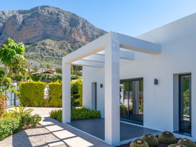 Extérieur moderne de la villa avec pergola blanche, jardin méditerranéen et vues dégagées sur l'imposante montagne du Montgó.