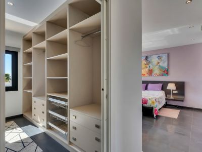 Grand dressing avec étagères intégrées, tiroirs et paniers coulissants, attenant à une chambre aux murs lavande et œuvre d'art murale.