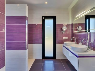 Salle de bain contemporaine avec carrelage mural violet et blanc, double vasque flottante avec lavabos ovales et miroir éclairé. Une porte en verre dépoli assure l'intimité.