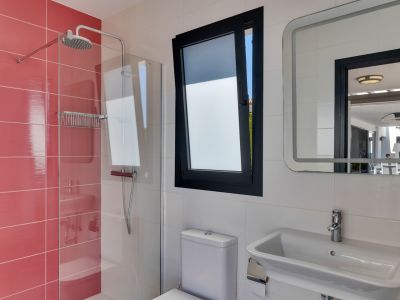Salle de bain fonctionnelle avec douche à l'italienne carrelée en rouge, fenêtre oscillo-battante et miroir lumineux reflétant la terrasse extérieure.