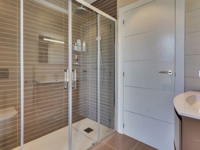 Salle de bain moderne avec douche à l'italienne spacieuse, paroi vitrée, pommeau de pluie et carrelage taupe à rayures horizontales. Comprend des toilettes suspendues et un meuble-lavabo.