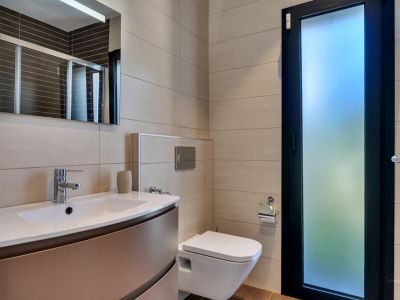 Salle de bain moderne avec WC suspendu, meuble vasque intégré, robinetterie chromée et carrelage mural neutre. Porte vitrée dépolie pour une lumière naturelle.