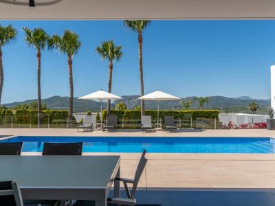 Terrasse couverte avec table à manger extérieure, offrant une vue sur la piscine carrelée de bleu, les palmiers et les montagnes lointaines.