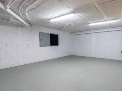Vaste espace inférieur ouvert avec murs en blocs blancs, sol gris clair et installations de plafond apparentes, éclairé par des néons.