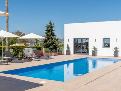 Vaste terrasse avec mobilier d'extérieur clair, piscine bleue invitante et vue sur la végétation luxuriante, propice à la détente.