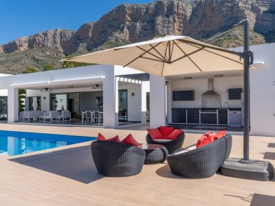 Vaste terrasse avec piscine, coin salon et cuisine extérieure équipée, encadrée par l'imposante montagne du Montgó sous un ciel bleu clair.