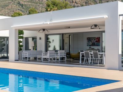 Vaste terrasse couverte avec store rétractable, salon et salle à manger extérieurs, attenante à la piscine et à l'intérieur, vue montagne.