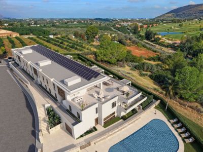 Vue aérienne d'une résidence de luxe moderne avec panneaux solaires sur le toit, terrasses extérieures avec salons et salles à manger, et une grande piscine, entourée d'un golf et de vergers.