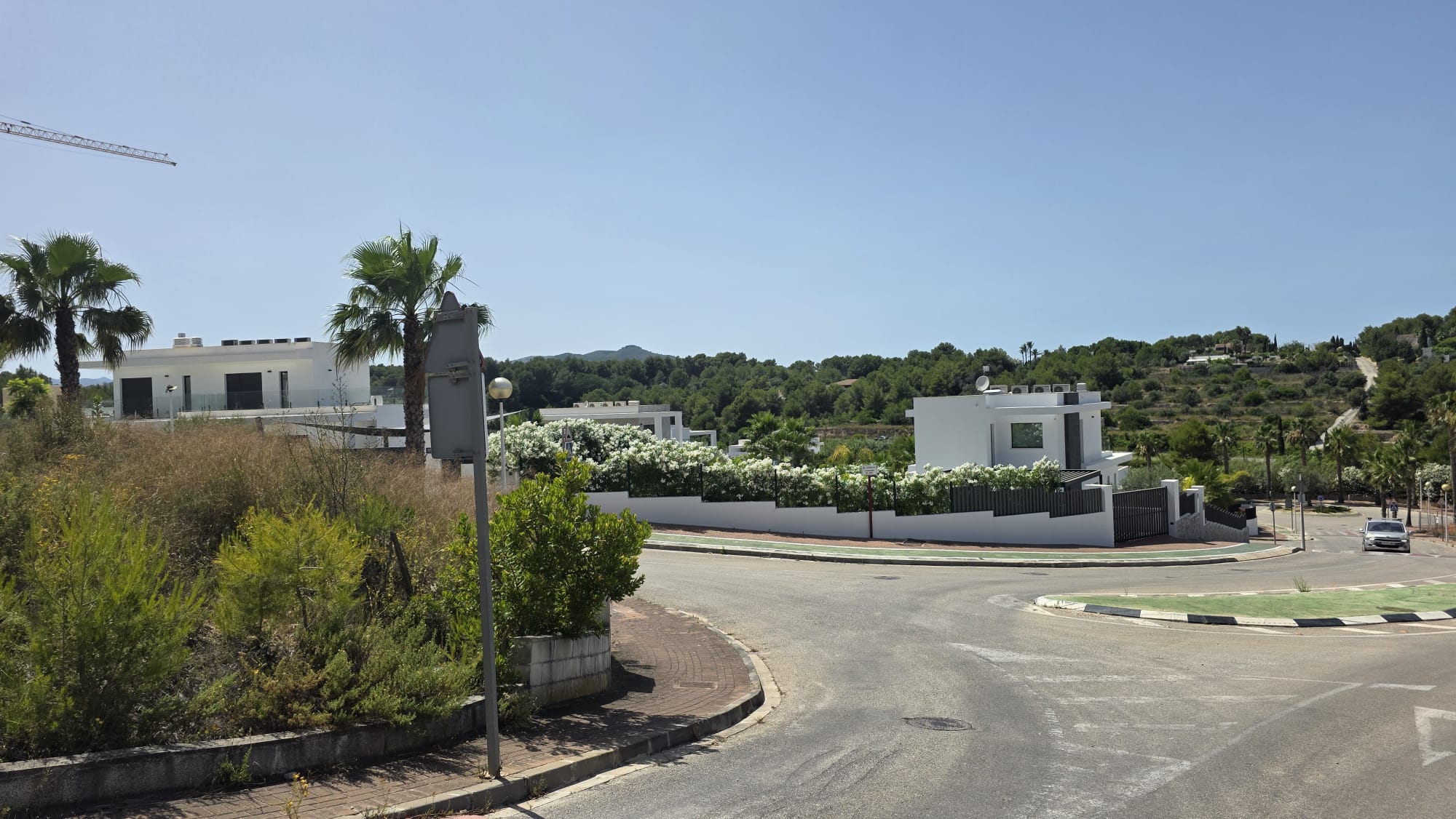 Scène de rue résidentielle montrant des villas blanches modernes avec balcons vitrés, entourées de flore méditerranéenne et de collines verdoyantes. Infrastructures routières et ciel clair. Scène de rue résidentielle montrant des villas blanches modernes avec balcons vitrés, entourées de flore méditerranéenne et de collines verdoyantes. Infrastructures routières et ciel clair.