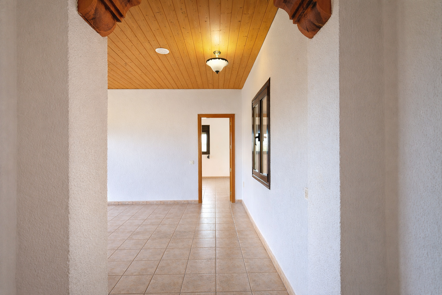 Couloir intérieur avec carrelage clair et murs blancs texturés. Plafond en bois clair avec luminaire central et détails sculptés à l'entrée. Couloir intérieur avec carrelage clair et murs blancs texturés. Plafond en bois clair avec luminaire central et détails sculptés à l'entrée.