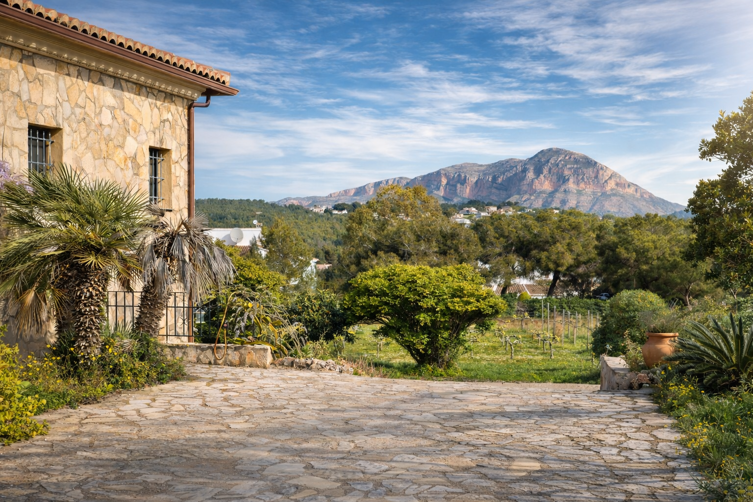 Façade en pierre rustique de la finca avec palmiers, allée pavée et vues sur le Montgó, entourée de vignobles et végétation méditerranéenne. Façade en pierre rustique de la finca avec palmiers, allée pavée et vues sur le Montgó, entourée de vignobles et végétation méditerranéenne.