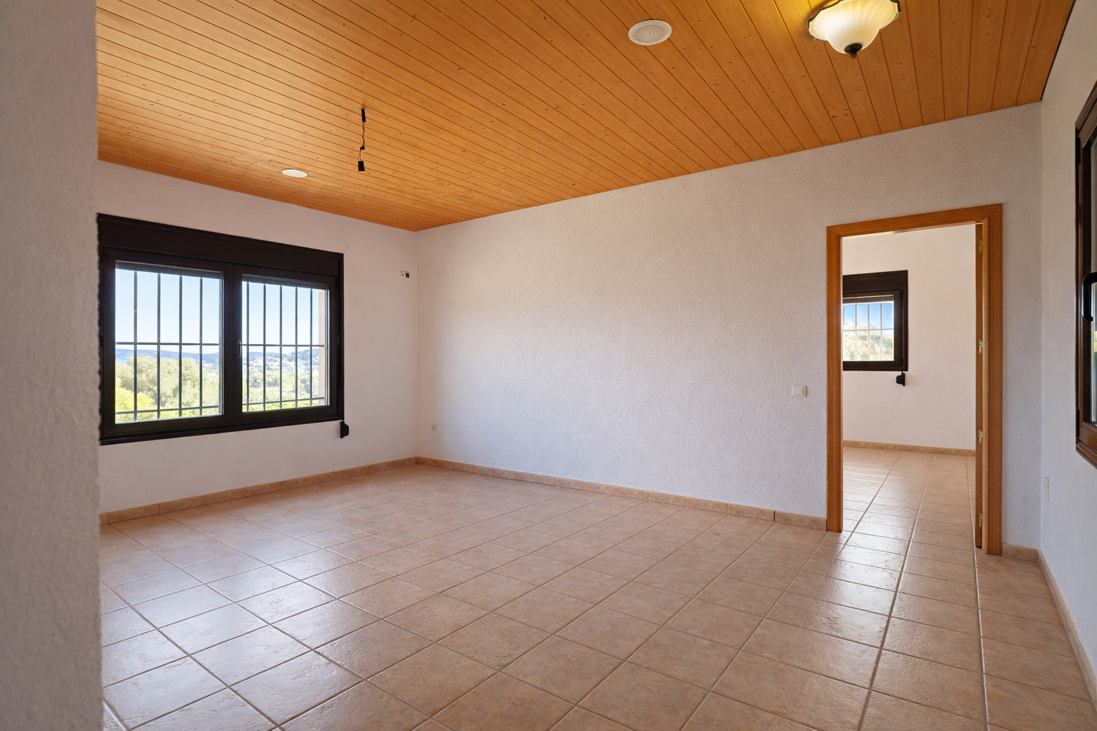 Pièce spacieuse avec carrelage clair, murs blancs texturés et plafond en bois lambrissé. Les fenêtres à barreaux offrent une vue dégagée sur la vallée et une lumière naturelle. Pièce spacieuse avec carrelage clair, murs blancs texturés et plafond en bois lambrissé. Les fenêtres à barreaux offrent une vue dégagée sur la vallée et une lumière naturelle.