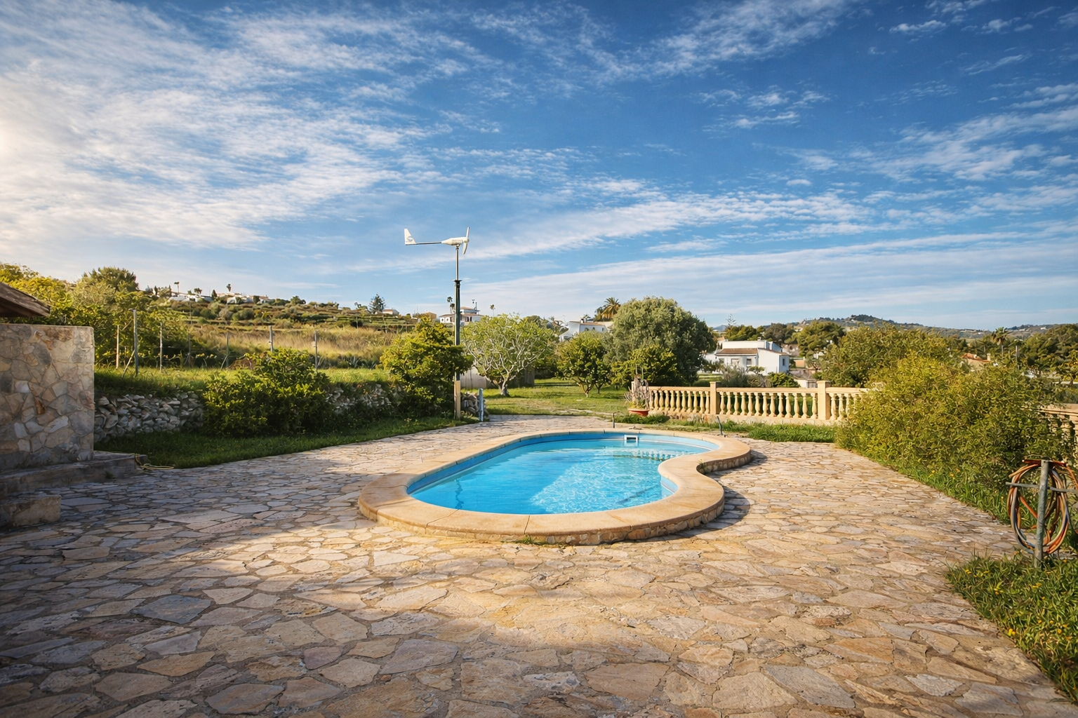 Piscine de forme organique sur une vaste terrasse en dalles de pierre irrégulières. Des collines verdoyantes et une éolienne compacte sont visibles à l'arrière-plan. Piscine de forme organique sur une vaste terrasse en dalles de pierre irrégulières. Des collines verdoyantes et une éolienne compacte sont visibles à l'arrière-plan.
