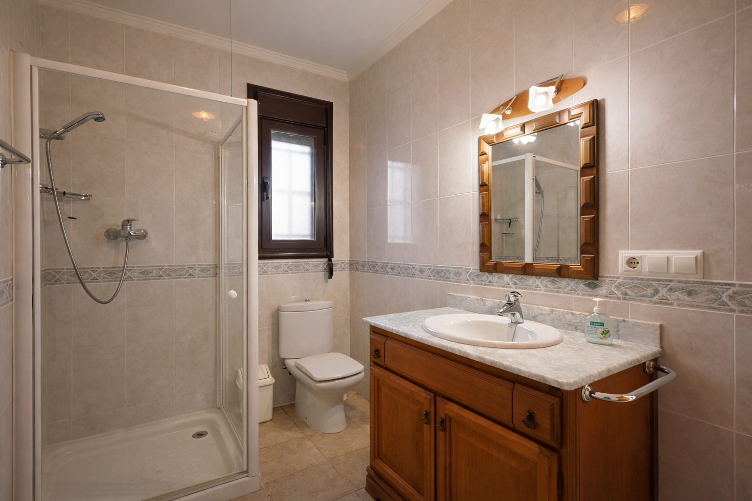 Salle de bain équipée d'une douche vitrée, de toilettes et d'un meuble-lavabo en bois avec un plan de travail en marbre. Les murs sont carrelés de tons clairs. Salle de bain équipée d'une douche vitrée, de toilettes et d'un meuble-lavabo en bois avec un plan de travail en marbre. Les murs sont carrelés de tons clairs.