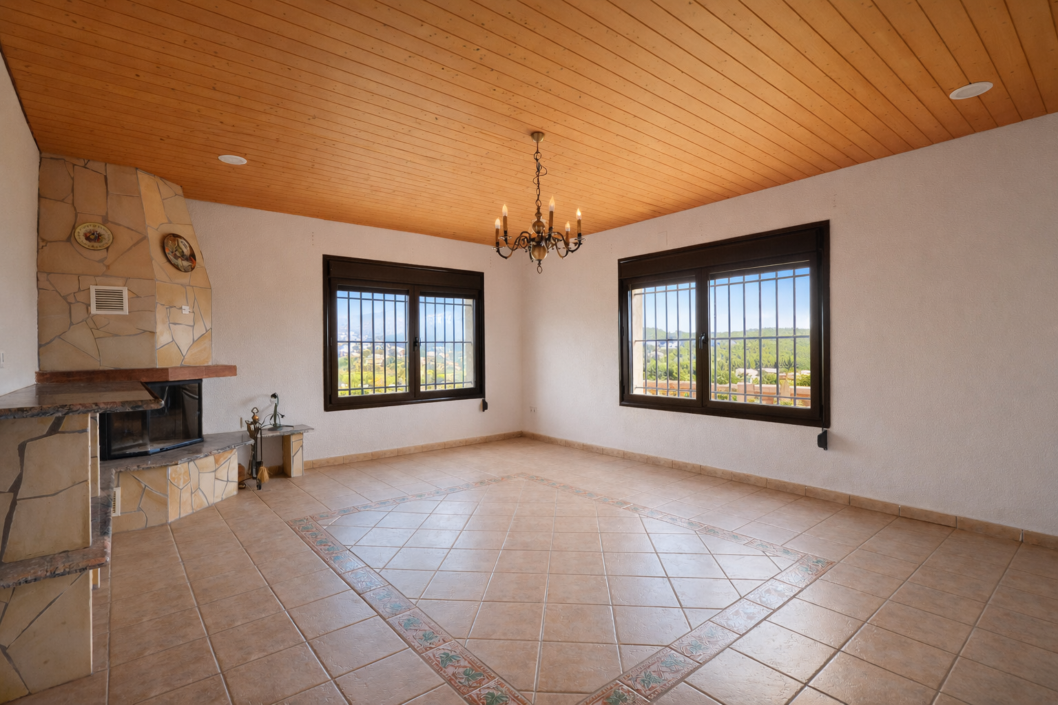 Vaste pièce avec cheminée en pierre, plafond en lattes de bois et sol carrelé à motif central décoratif. Deux fenêtres à barreaux offrent des vues sur la vallée. Vaste pièce avec cheminée en pierre, plafond en lattes de bois et sol carrelé à motif central décoratif. Deux fenêtres à barreaux offrent des vues sur la vallée.