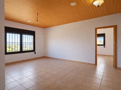Pièce spacieuse avec carrelage clair, murs blancs texturés et plafond en bois lambrissé. Les fenêtres à barreaux offrent une vue dégagée sur la vallée et une lumière naturelle.