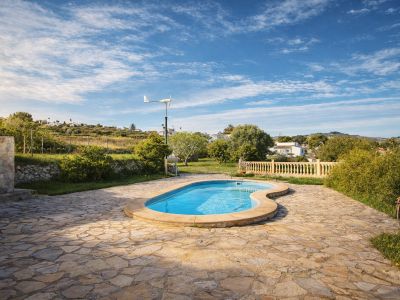 Piscine de forme organique sur une vaste terrasse en dalles de pierre irrégulières. Des collines verdoyantes et une éolienne compacte sont visibles à l'arrière-plan.