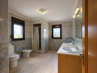 Salle de bain spacieuse avec double vasque sur plan de travail en marbre et meuble en bois. Elle comprend une douche à l'italienne, des toilettes, un bidet et deux fenêtres.