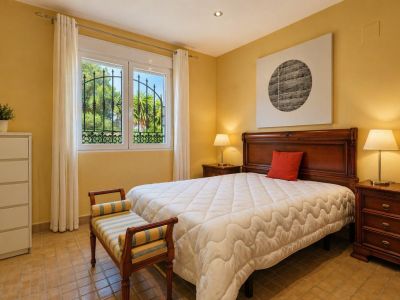 Chambre lumineuse avec lit en bois massif, tables de chevet assorties et carrelage en terre cuite. La fenêtre à barreaux en fer forgé donne sur le jardin.