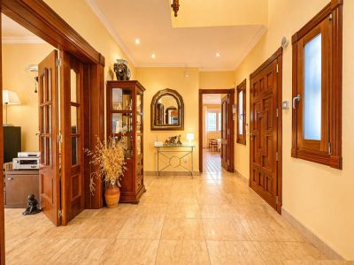 Couloir lumineux aux murs jaune chaud et carrelage clair. Il présente des portes en bois foncé, une vitrine décorative et une console avec un miroir arqué.