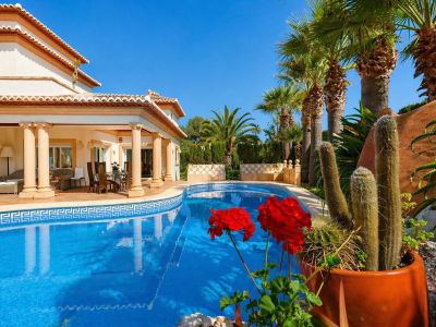La piscine accueillante avec sa frise en mosaïque grecque encadre une vaste terrasse couverte, avec élégants espaces repas et salon extérieurs, entourée de palmiers et cactus méditerranéens.