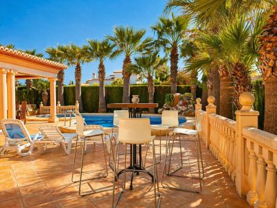 Le patio extérieur privé offre une table haute avec tabourets, des chaises longues et une balustrade sur carreaux de terre cuite. La piscine est bordée de palmiers matures et d'une haie luxuriante.