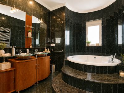 Salle de bain élégante avec carrelage effet marbre vert foncé, baignoire courbe encastrée sur des marches en pierre et double vasque en verre sur meuble en bois.