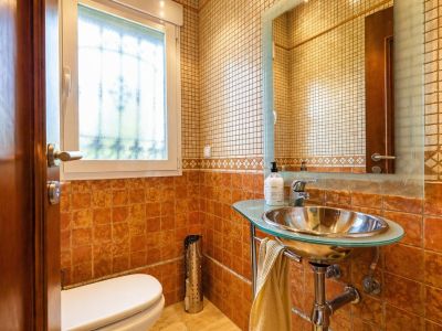 Toilettes d'invités avec carrelage terre cuite et mosaïque, lavabo design à vasque métallique et plateau en verre, et fenêtre lumineuse.