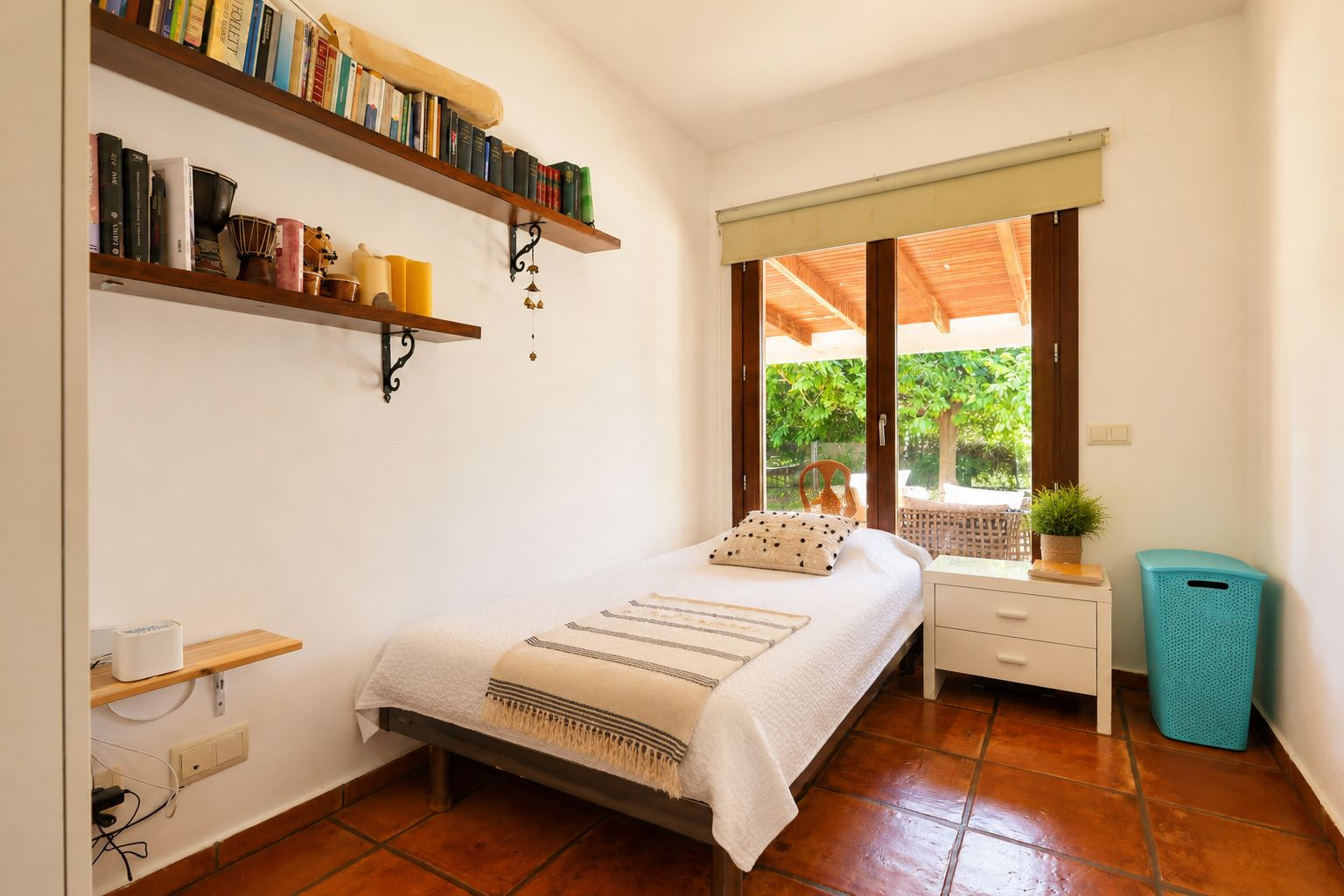 Chambre individuelle avec carrelage en terre cuite, murs blancs et accès direct à une terrasse couverte par une grande porte vitrée en bois. Des étagères murales avec des livres sont visibles. Chambre individuelle avec carrelage en terre cuite, murs blancs et accès direct à une terrasse couverte par une grande porte vitrée en bois. Des étagères murales avec des livres sont visibles.