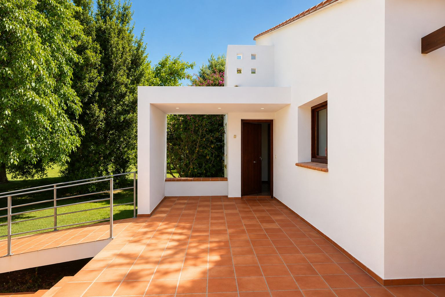 Patio d'entrée principal couvert avec carrelage en terre cuite et éclairage encastré. Une rampe accessible mène au jardin verdoyant, s'harmonisant avec la façade blanche. Patio d'entrée principal couvert avec carrelage en terre cuite et éclairage encastré. Une rampe accessible mène au jardin verdoyant, s'harmonisant avec la façade blanche.