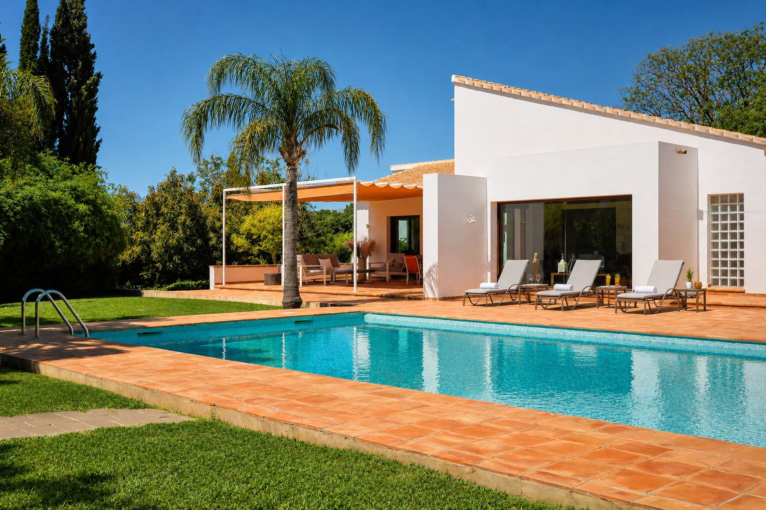 Piscine carrelée de bleu et entourée de terre cuite, bordée d'une pelouse verte. Des chaises longues sont disposées devant la façade blanche de la maison, près d'une pergola ombragée. Piscine carrelée de bleu et entourée de terre cuite, bordée d'une pelouse verte. Des chaises longues sont disposées devant la façade blanche de la maison, près d'une pergola ombragée.
