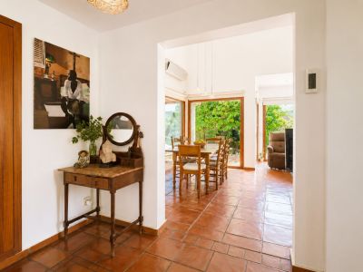 L'entrée lumineuse, avec son sol en terre cuite et sa console vintage, mène à une salle à manger spacieuse dotée de grandes fenêtres donnant sur le jardin luxuriant.