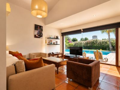 Vaste salon avec carrelage en terre cuite et accès direct à la piscine. La pièce bénéficie d'une lumière naturelle abondante, de sièges confortables et d'une vue sur le jardin et une tour lointaine.