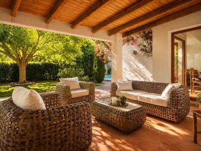 Vaste terrasse couverte avec plafond à poutres en bois et carrelage en terre cuite, aménagée avec des meubles tressés et offrant un accès direct au jardin luxuriant et à la piscine.