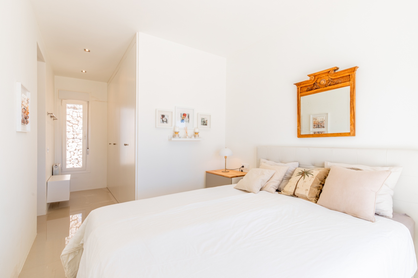 Chambre lumineuse avec lit blanc, tête de lit capitonnée et table de chevet en bois. Un miroir orné et un couloir avec fenêtre étroite donnant sur un mur de pierre. Chambre lumineuse avec lit blanc, tête de lit capitonnée et table de chevet en bois. Un miroir orné et un couloir avec fenêtre étroite donnant sur un mur de pierre.