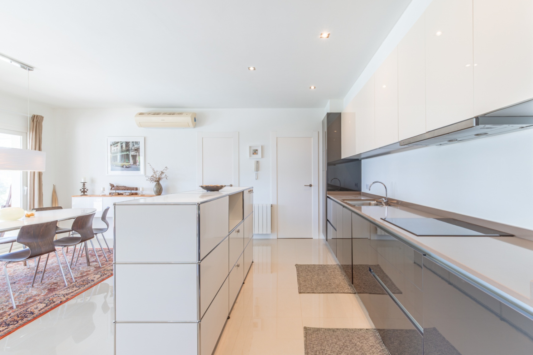 Cuisine moderne ouverte avec des armoires laquées blanches et gris foncé, une plaque à induction intégrée et un îlot modulaire. Coin repas adjacent avec table ovale et chaises en bois. Cuisine moderne ouverte avec des armoires laquées blanches et gris foncé, une plaque à induction intégrée et un îlot modulaire. Coin repas adjacent avec table ovale et chaises en bois.