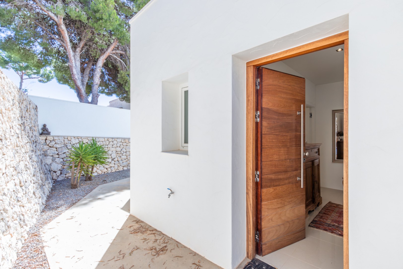 Entrée principale avec une porte moderne en bois massif, encadrée par des murs blancs et un mur en pierres sèches. Un chemin en béton mène au hall d'entrée lumineux. Entrée principale avec une porte moderne en bois massif, encadrée par des murs blancs et un mur en pierres sèches. Un chemin en béton mène au hall d'entrée lumineux.