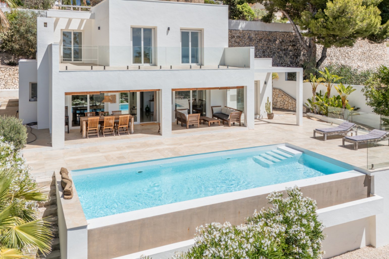 Extérieur de villa moderne avec piscine rectangulaire à marches et vaste terrasse en pierre claire. Comprend un coin repas extérieur, un salon et un balcon supérieur avec garde-corps en verre. Extérieur de villa moderne avec piscine rectangulaire à marches et vaste terrasse en pierre claire. Comprend un coin repas extérieur, un salon et un balcon supérieur avec garde-corps en verre.