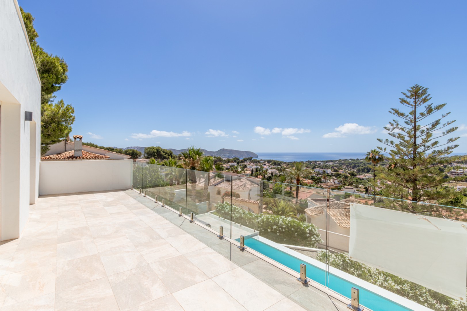 Grande terrasse extérieure carrelée de couleur claire avec balustrade en verre. Vues panoramiques sur la Méditerranée, la baie et le paysage urbain, avec piscine étroite et végétation. Grande terrasse extérieure carrelée de couleur claire avec balustrade en verre. Vues panoramiques sur la Méditerranée, la baie et le paysage urbain, avec piscine étroite et végétation.