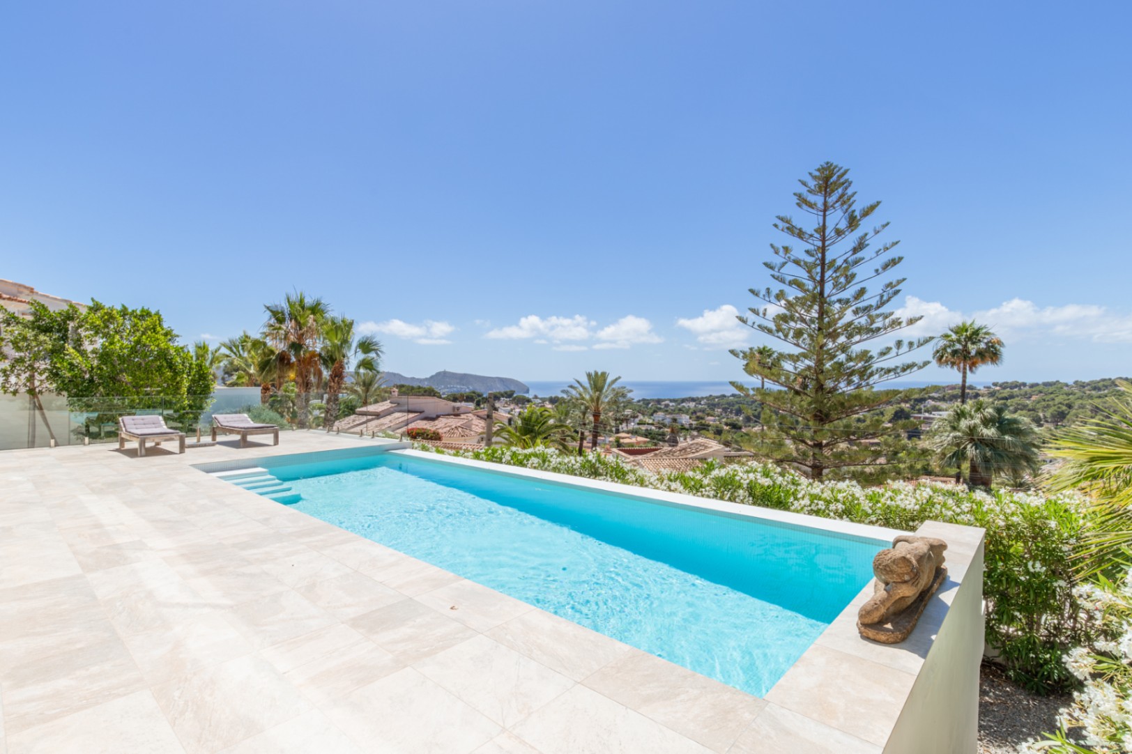 Piscine à débordement carrelée de bleu clair, terrasse en grès beige et vue panoramique sur la mer Méditerranée. Deux chaises longues et une végétation méditerranéenne luxuriante. Piscine à débordement carrelée de bleu clair, terrasse en grès beige et vue panoramique sur la mer Méditerranée. Deux chaises longues et une végétation méditerranéenne luxuriante.