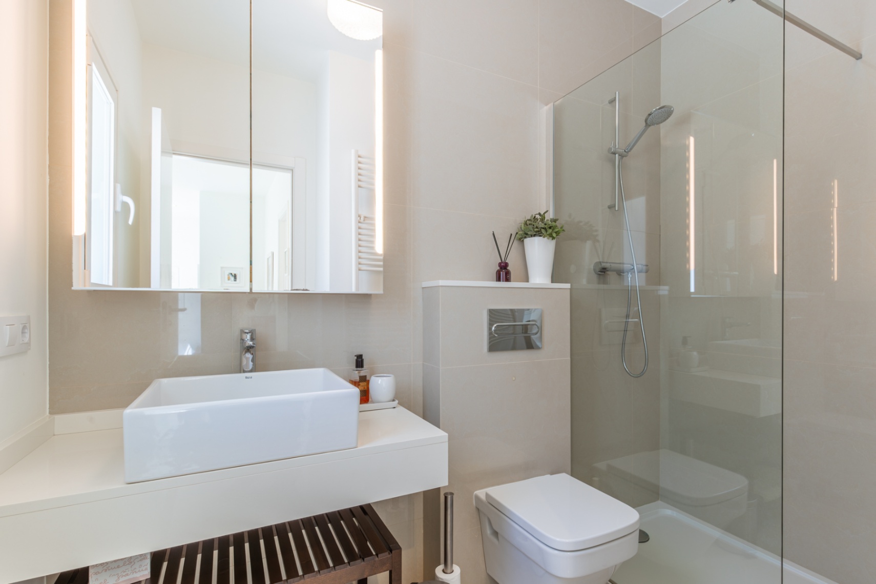 Salle de bain moderne avec lavabo rectangulaire sur meuble suspendu, miroir éclairé par LED et douche vitrée. Revêtement mural en carreaux neutres. Salle de bain moderne avec lavabo rectangulaire sur meuble suspendu, miroir éclairé par LED et douche vitrée. Revêtement mural en carreaux neutres.