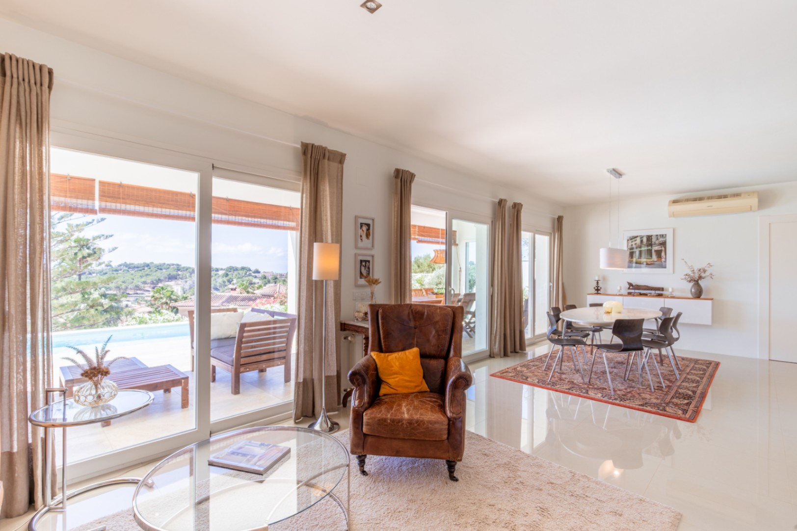 Salon-salle à manger ouvert avec de grandes baies vitrées donnant sur la terrasse, la piscine et le paysage. Carrelage blanc brillant et mobilier moderne. Salon-salle à manger ouvert avec de grandes baies vitrées donnant sur la terrasse, la piscine et le paysage. Carrelage blanc brillant et mobilier moderne.