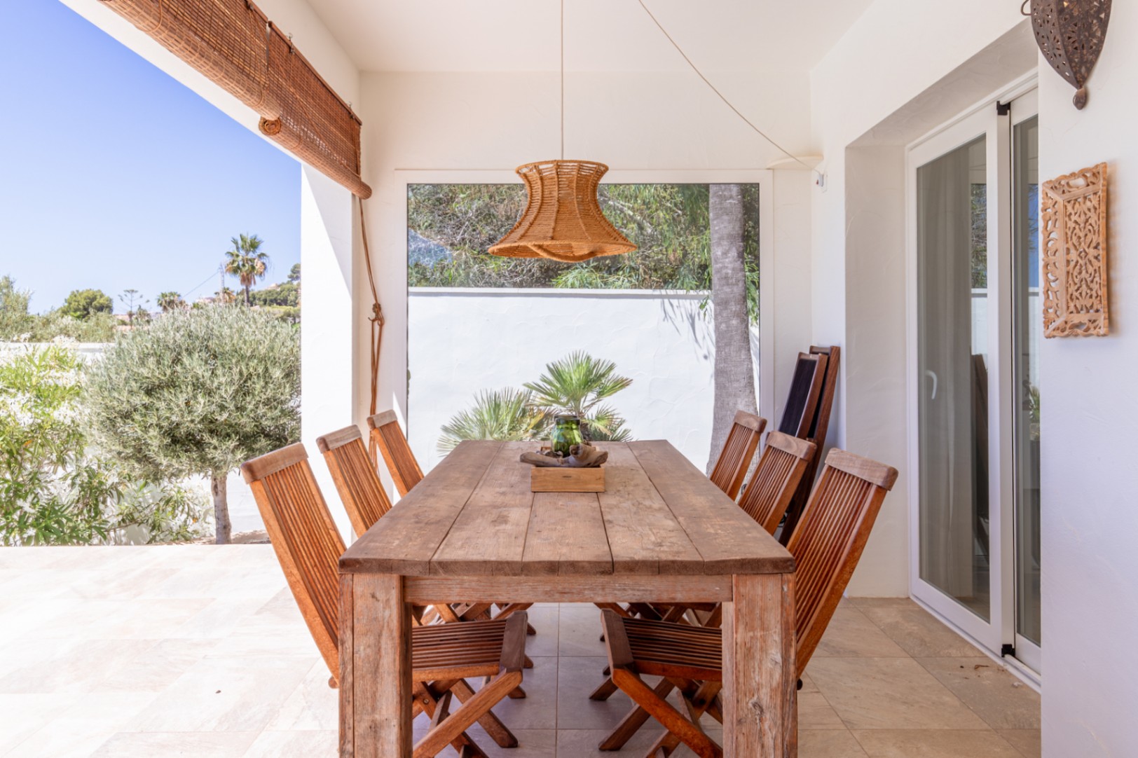 Terrasse couverte avec table et chaises en bois rustique, éclairée par une suspension tressée. Vues directes sur la verdure méditerranéenne luxuriante. Terrasse couverte avec table et chaises en bois rustique, éclairée par une suspension tressée. Vues directes sur la verdure méditerranéenne luxuriante.