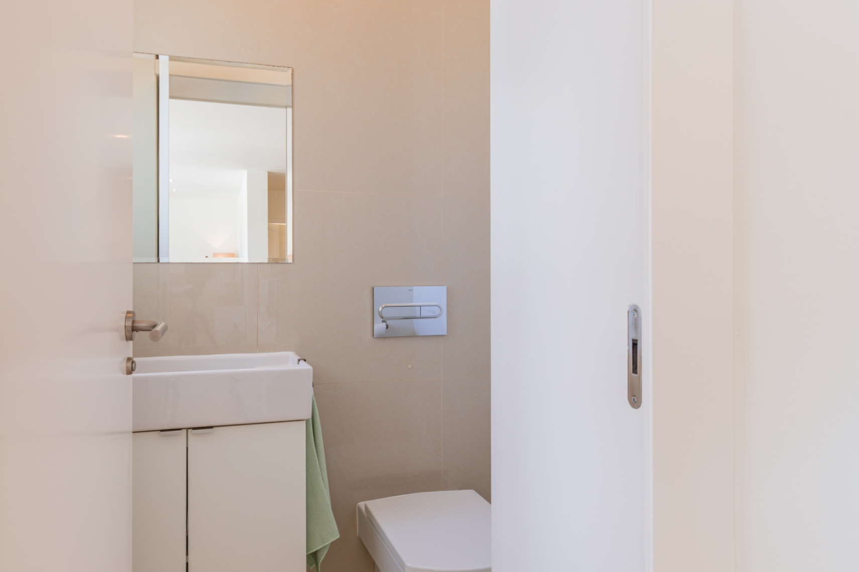 Toilettes modernes avec lavabo rectangulaire et meuble sous-vasque blanc, miroir mural et WC suspendu. Les murs sont recouverts de carrelage beige clair. Toilettes modernes avec lavabo rectangulaire et meuble sous-vasque blanc, miroir mural et WC suspendu. Les murs sont recouverts de carrelage beige clair.