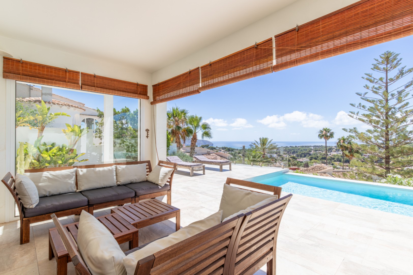 Vaste terrasse couverte avec mobilier de salon en bois, carrelage clair et piscine à débordement, offrant une vue panoramique sur la Méditerranée. Vaste terrasse couverte avec mobilier de salon en bois, carrelage clair et piscine à débordement, offrant une vue panoramique sur la Méditerranée.