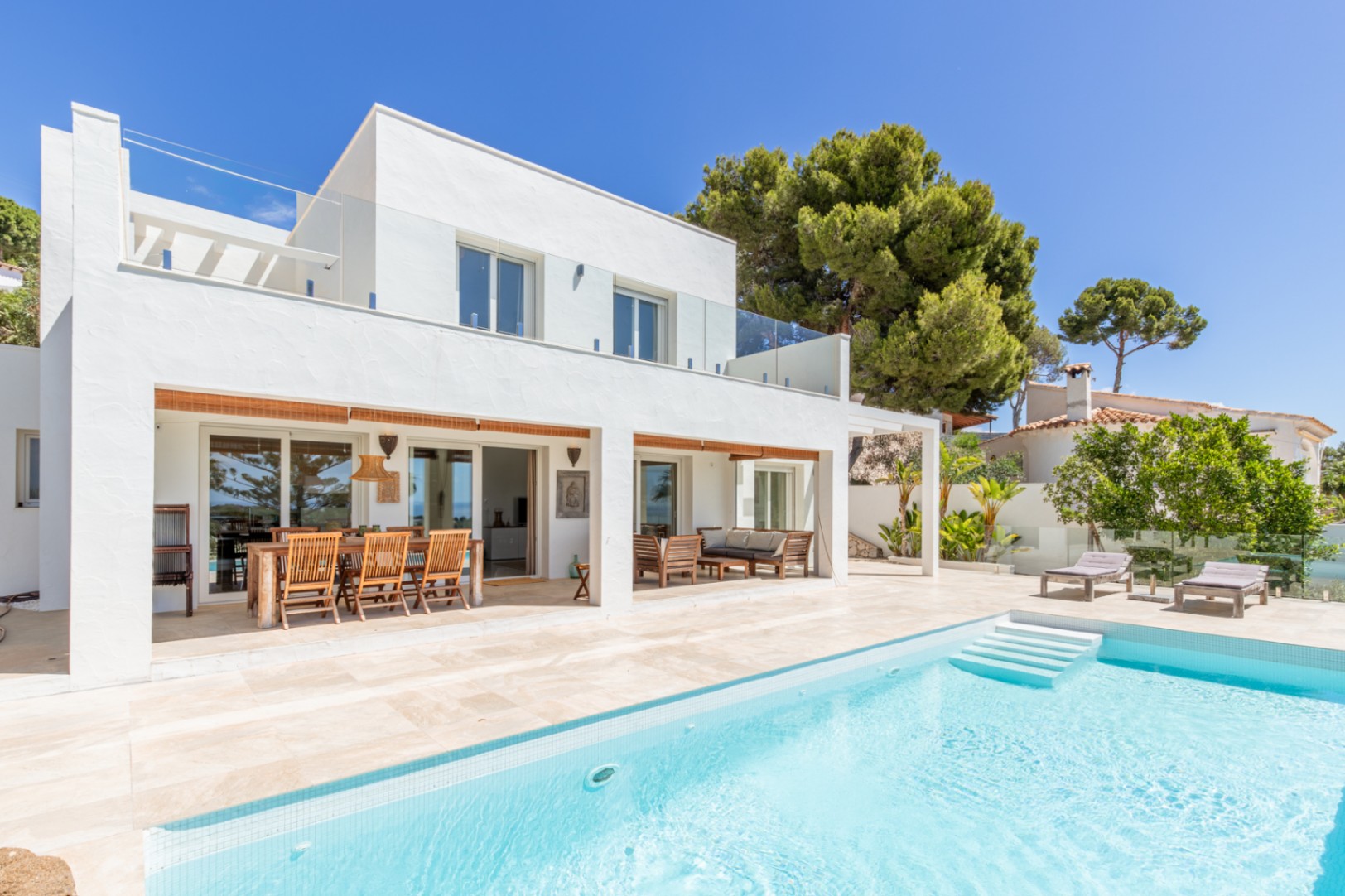 Villa moderne avec piscine carrelée claire et vastes terrasses. Elle dispose d'un coin repas extérieur couvert, d'un espace salon et de balustrades en verre à l'étage. Villa moderne avec piscine carrelée claire et vastes terrasses. Elle dispose d'un coin repas extérieur couvert, d'un espace salon et de balustrades en verre à l'étage.
