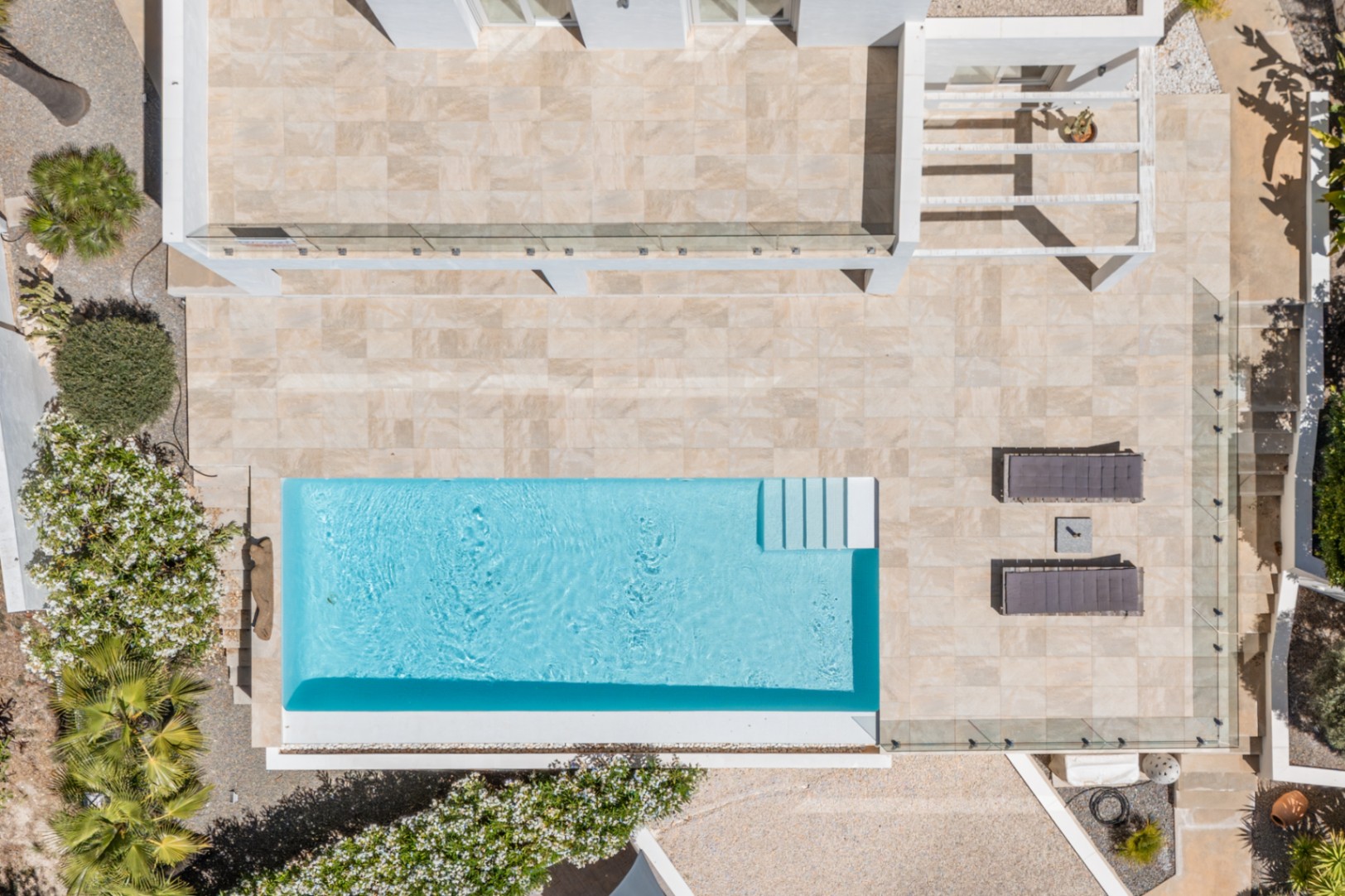 Vue aérienne de la piscine rectangulaire bleue, entourée d'une vaste terrasse carrelée claire, avec transats et végétation méditerranéenne. Vue aérienne de la piscine rectangulaire bleue, entourée d'une vaste terrasse carrelée claire, avec transats et végétation méditerranéenne.